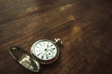 Vintage round pocket watch on a wooden table. Nostalgia for a bygone time.