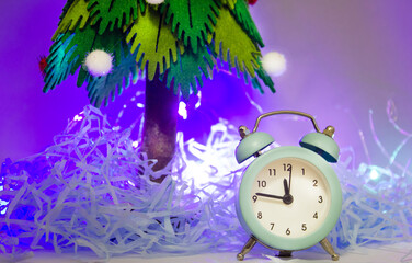 blue alarm clock against the background of a green Christmas tree, the new year is coming soon. 2023