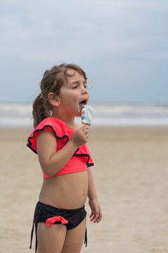 Crian&ccedil;a de 3 anos feliz tomando sorvete na praia. Menina usando biquini cor de rosa saboreando um delicioso sorvete na praia. Espa&ccedil;o para texto e fundo desfocad0.
