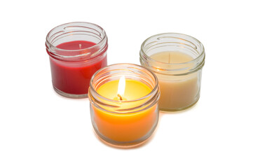 a set of multicolored scented candles with one lit in glass jars on a white background