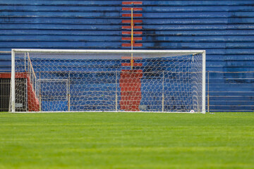 Fototapeta premium Beam of a football field with the base of the image with green grass, in the background the bleachers, without people, painted in red and blue. 