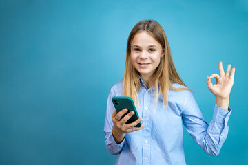 Girl with a phone in her hands shows ok on a blue background