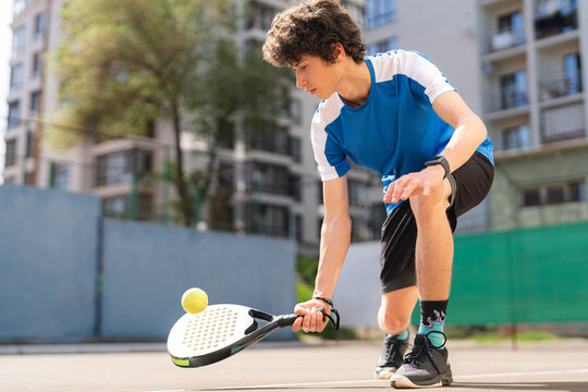Sportive young boy with racquet playing padel in the open court outdoors