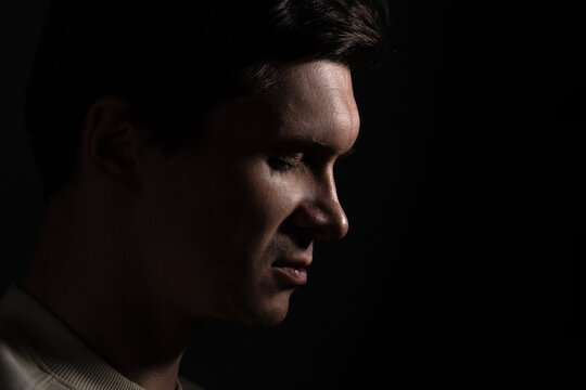 profile of thoughtful man looks to the right. portrait in side light, hard light, photo on black, looks down