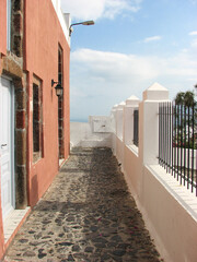 A beautiful stone walkway beside a white wall and a pink house on Santorini Island, Greece. Image has copy space.