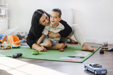 Kid with health problem playing toy cars with mother at home. child having Cerebral palsy entertaining on mat with caregiver Inclusion, rehabilitation in family for people with special needs