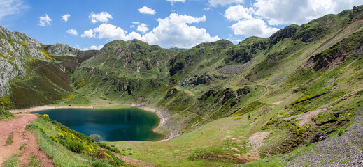 Fototapeta na wymiar Vistas del paisaje asturiano del Lago de La Cueva por un sendero rodeado de naturaleza, montañas verdes, flores moradas cielo azul y nubes blancas en verano de 2021, España. 
