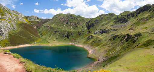 Vistas del paisaje asturiano del Lago de La Cueva por un sendero rodeado de naturaleza, montañas verdes, flores moradas cielo azul y nubes blancas en verano de 2021, España. 