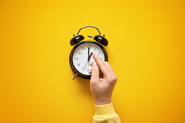 Daylight saving day. Fall Back. Black Alarm clock and female hands on yellow background. Daylight saving time end - obrazy, fototapety, plakaty