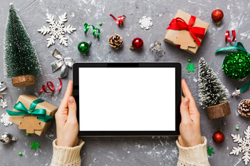 Christmas online shopping from home, female hands holding tablet pc with blank white display top view. woman hand holding tablet with blank screen, Christmas tree and gifts on background