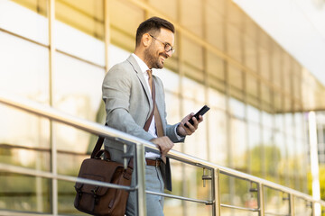 Portrait of a young business man in front of office building holding phone and looking away