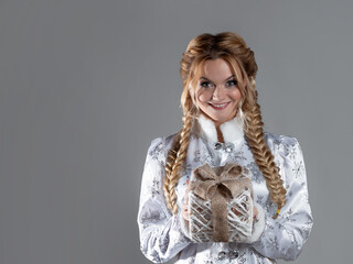 beautiful snow maiden with long braids in a silver fur coat holds a gift box in her hands, happy...
