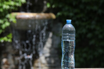 A bottle of water on the background of a fountain with falling drops in the form of a bokeh.The concept of a refreshing drink and recuperation