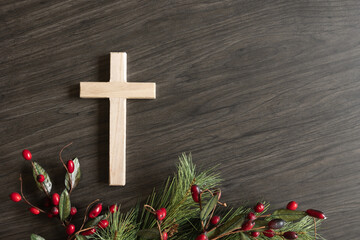 Simple wood cross with border of evergreen boughs and red berries on a dark wood background with copy space