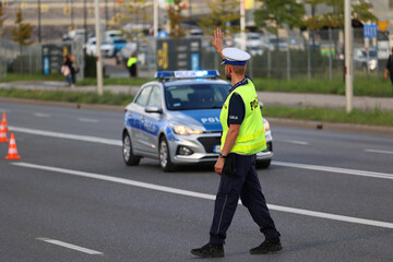 Policjant ruchu drogowego przy swoim radiowozie kontroluje ruch drogowy w mieście. - obrazy, fototapety, plakaty