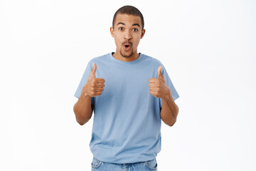 Smiling arab man shows thumbs up, recommends, gives positive feedback and his approval, stands over white background