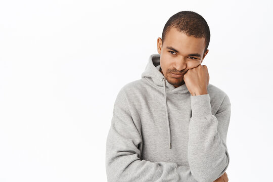 Bored or uspet young man, lean head on arm and looking disappointed, gloomy at camera, standing over white background