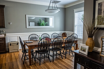 A large dining room with a simple farmhouse tabel and chairs, a window, mirror and wood floors