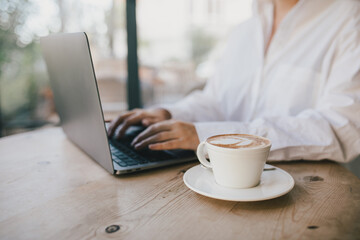 Young woman drinking coffee working online using her laptop.