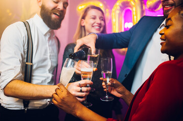 People hands holding flute glasses while pouring champagne