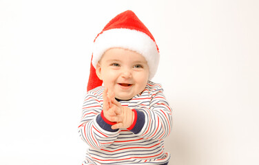 Adorable child is sitting on floor, wearing red Christmas cap, isolated over white background.