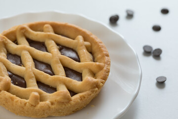 Crostata al cioccolato su piattino e tavolo bianco con gocce di cioccolato