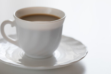 Tazza bianca con caffè e piattino su tavolo bianco