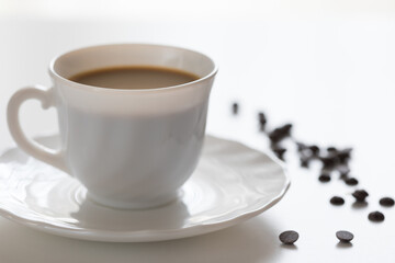 Tazza bianca con caffè e piattino con chicchi di cioccolato su tavolo bianco
