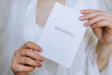 The bride in her hands holds a white envelope, an invitation, a gift sheet of paper. Close-up wedding photography, copy space, portrait.