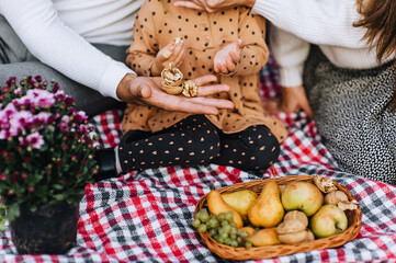 A happy, loving family sits on a plaid with a walnut in their hands close-up. Photo of father, mother and child, daughter in nature in the forest at a picnic with a basket of fruits.