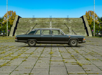 An old black vintage retro russian GAZ 14 Chaika limousine side view - with soviet style fancy stairscase blurred in the background