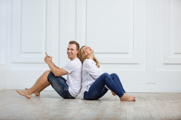Lovely young couple sitting on floor, leaning back to back and laughing