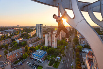 Rock climber hanging on element of roof of high building at sunset.
