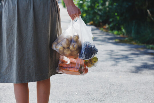 Woman holding plastic bags with fresh vegetables from farmer's market, walking on city street