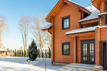 Scenery facade front view of modern wooden luxury timber eco house villa with garage door snowcapped by white fresh snow at cold sunny winter day. Real estate building construction project exterior