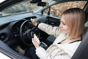 Fototapeta na wymiar Blond woman holding a phone with a navigator while sitting at the wheel of a car
