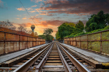 Obraz na płótnie Canvas as long set of rusty iron and wood railroad tracks surrounded by the Sunsphere and autumn colored trees and lush green trees with blue sky and powerful clouds at World's Fair Park in Knoxville