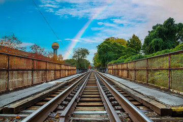 Fototapeta na wymiar as long set of rusty iron and wood railroad tracks surrounded by the Sunsphere and autumn colored trees and lush green trees with powerful clouds and a rainbow at World's Fair Park