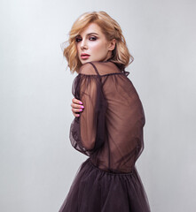 Fototapeta premium Alluring blond beautiful woman with curly short hair style posing in fashion black dress on blue background. Closeup studio portrait