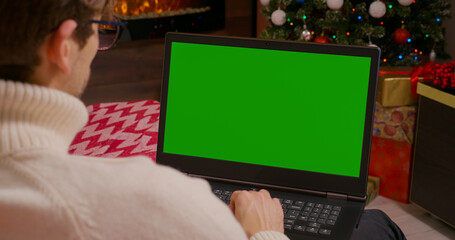 Over the Shoulder: Man Using Laptop with Mock-up Green Screen. Young Professionals Work on Computers on holidays. Succesful entrepreneurs. Typing on green laptop chroma key.