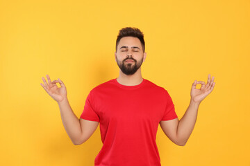Fototapeta premium Young man meditating on yellow background. Zen concept