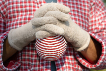 Stripped red and white christmas ball ornament in a green forest, hanging in a wood trunk, with a Santa's sequins hat. Perfect for a christmas market or party invitation or for a greetings card