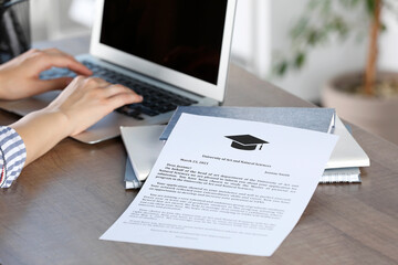 Student working with laptop at table indoors, focus on acceptance letter from university