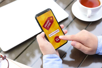 Man with smartphone activating promo code at wooden table outdoors, closeup