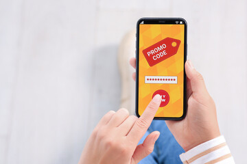 Woman activating promo code on smartphone against blurred background, closeup. Space for text