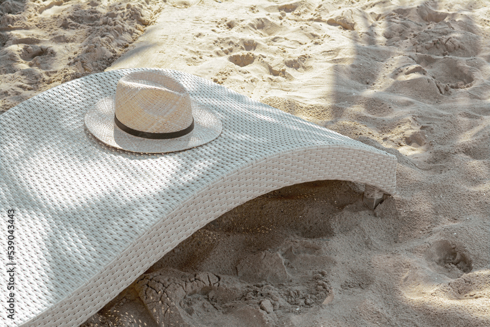 Wall mural Sunbed with stylish straw hat on sandy beach, space for text