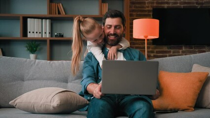 Cute active naughty girl noisy child plays with daddy hugs father distract parental attention disturbs parent from work on laptop at home single loving caucasian dad man calms down restless daughter
