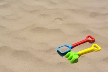 Fototapeta na wymiar Plastic shovel and rake on sand, space for text. Beach toys