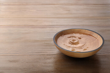 Drop falling down into bowl with clear water on wooden table. Space for text