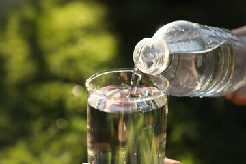 Pouring fresh water from bottle into glass outdoors, closeup